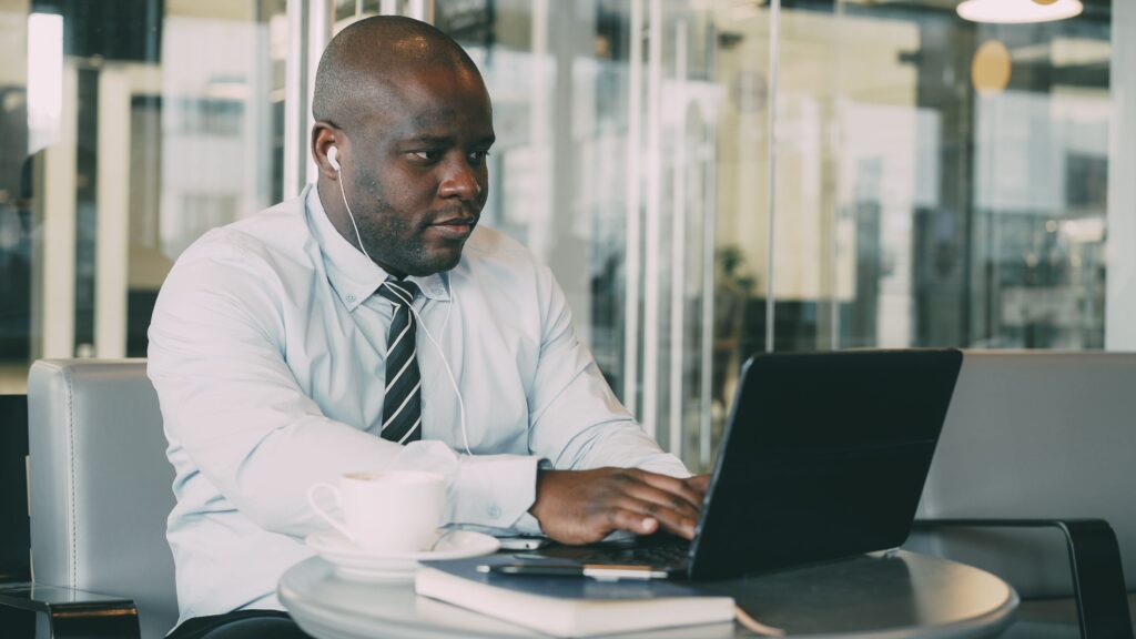 Business professional working on a laptop at a café table with coffee, wearing headphones.